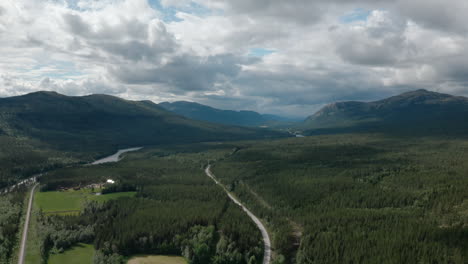 aerial view of green forest landscape with lone road stretching toward mountains in norway