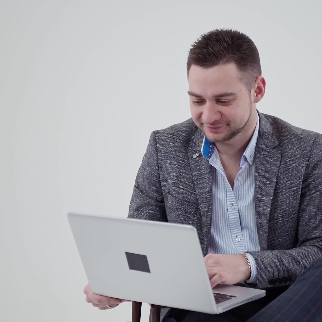 Businessman working on a laptop. Man in stylish costume looking into the laptop and becomes happy on white background. Slow motion.