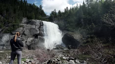 back view of a female tourist standing in front of chute neigette waterfall in rimouski, quebec, canada - wide shot