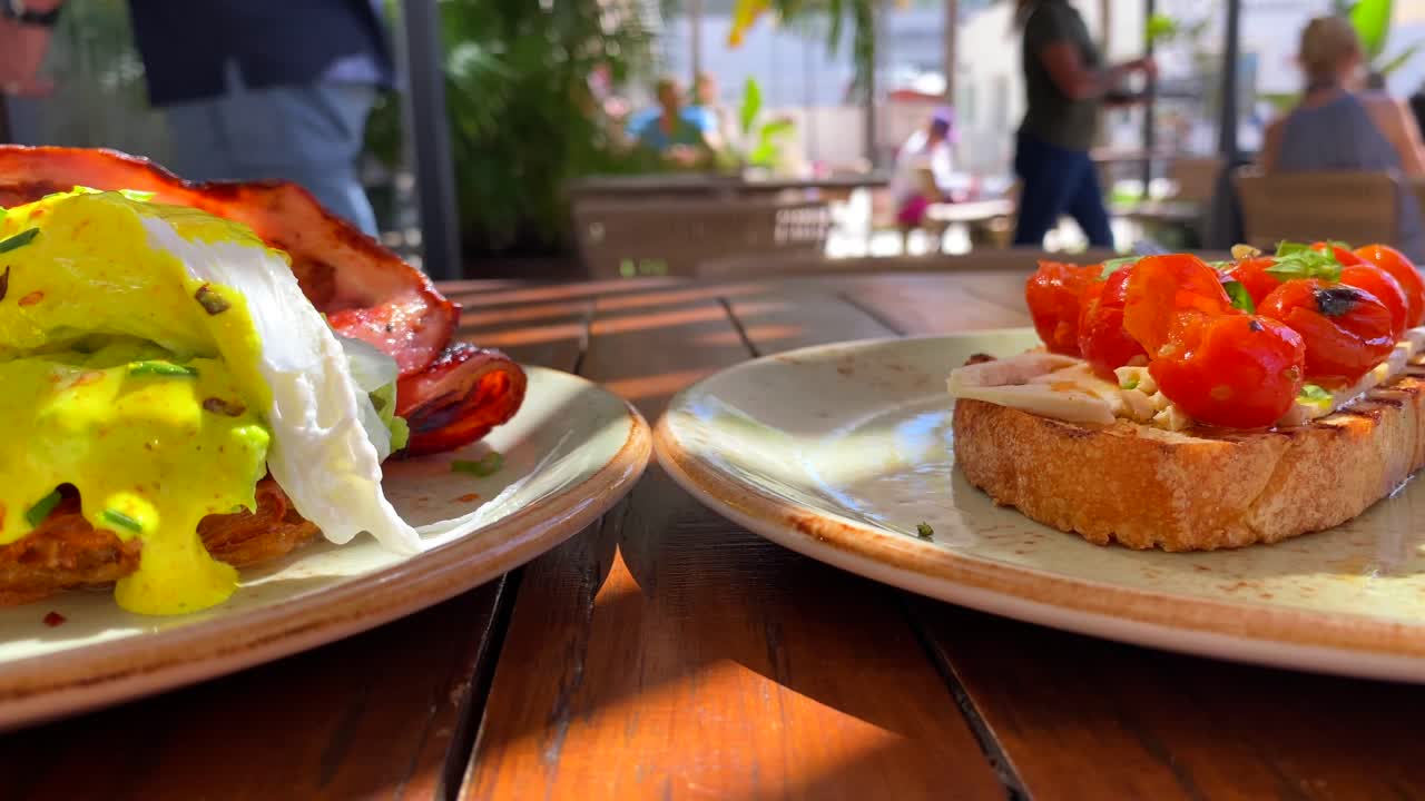 바삭한 베이컨, 홀랜다이즈 소스, 고구마 해시 브라운에 아보카도를 곁들인 맛있는 에그 베네딕트 조식 요리, 체리 토마토를 곁들인 브루스케타 토스트, 레스토랑에서 브런치로 데친 달걀, 4k