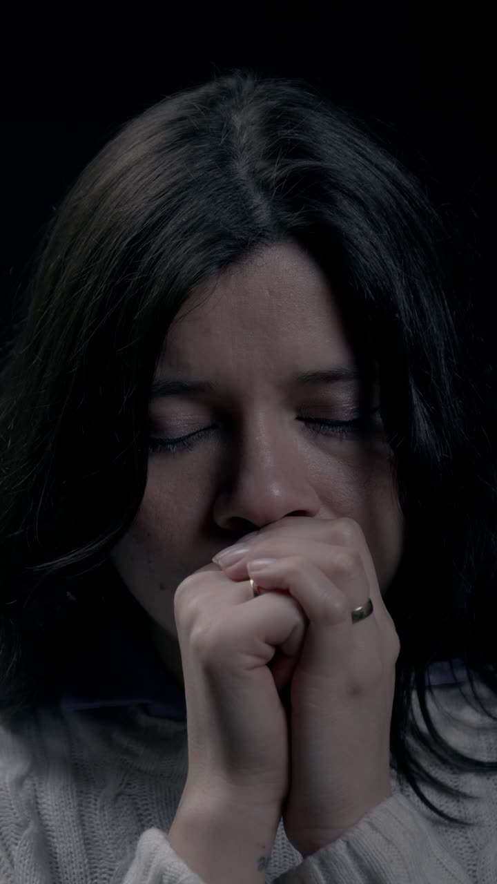 Close-up intimista de uma mulher hispânica orando, capturado em formato de vídeo vertical para visualização otimizada em dispositivos móveis. A iluminação suave enfatiza sua devoção e emoção durante este momento pessoal.