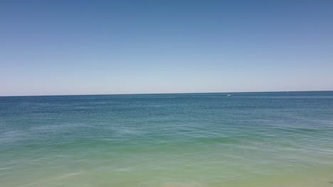 Aerial-forward-view-over-calm-ocean-heading-toward-small-boat