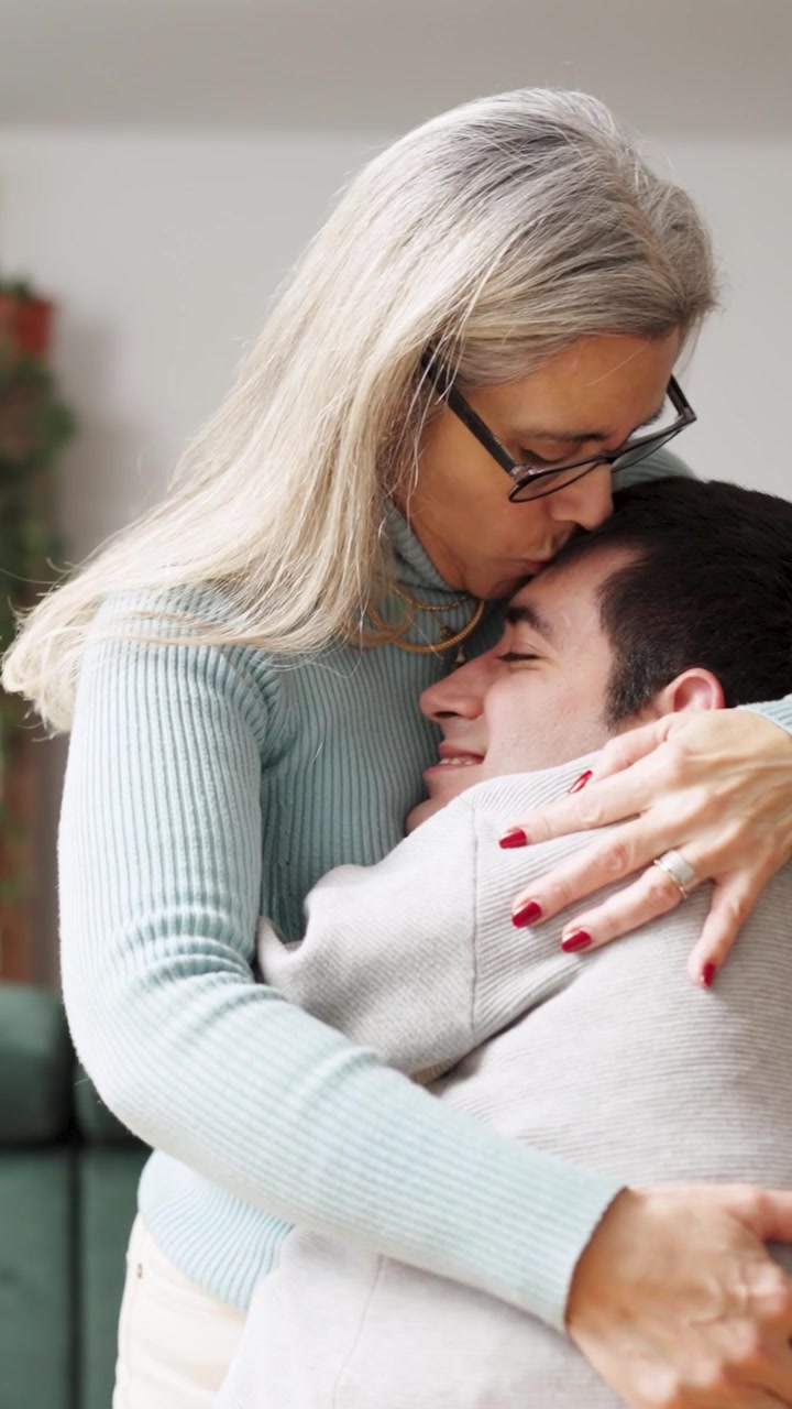 Donna matura che abbraccia e bacia il figlio adulto