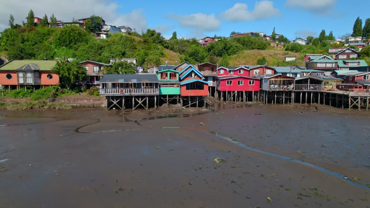 casas coloridas en una orilla fangosa durante la marea baja en castro, chiloé, con exuberante vegetación en el fondo