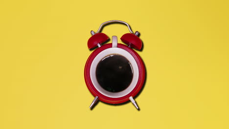 A-cup-of-dark-brown-hot-coffee-inside-a-red-alarm-clock,-over-a-yellow-background