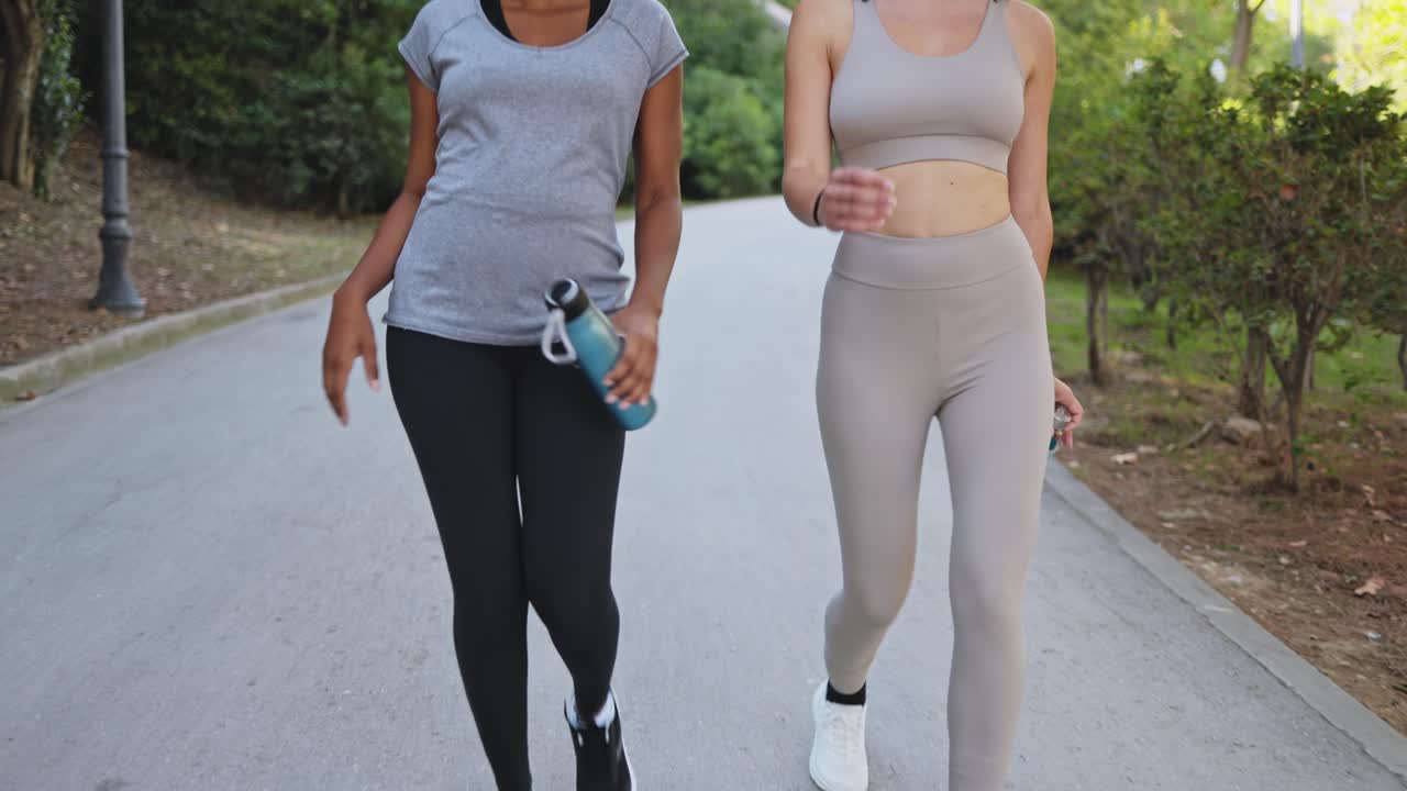 Due donne che camminano in un parco con bottiglie d'acqua