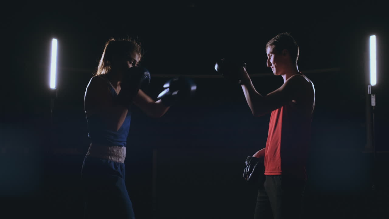 여성 권투 선수가 연기가 많은 체육관에서 권투 장갑으로 초점을 맞추고 있습니다.