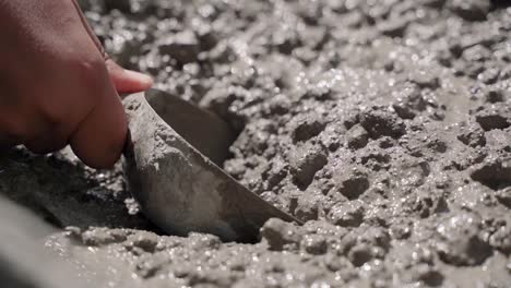 a male hand scoops up some cement mixed with gravel