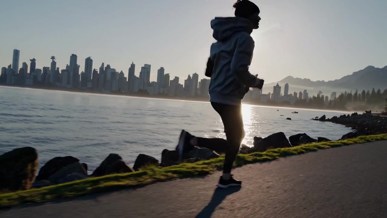 Silhouette of a Man Running Along the Waterfront at Sunrise with City Skyline