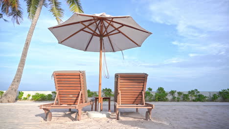 two empty beach loungers under a shade umbrella face out at an ocean view