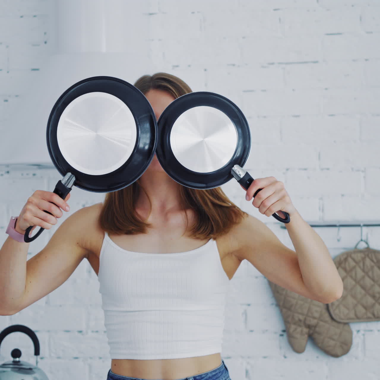 Woman with new frying pans in the kitchen. Beautiful female holding two empty black frying pans. Happy girl showing different emotions on her face in kitchen.