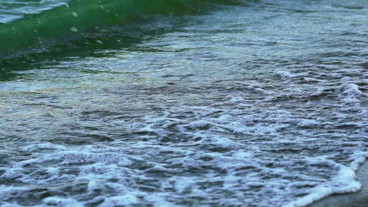 Sea water on the coastline. Waves crashing on the shore making foamy water. Amazing view on the edge of the ocean. Slow motion.