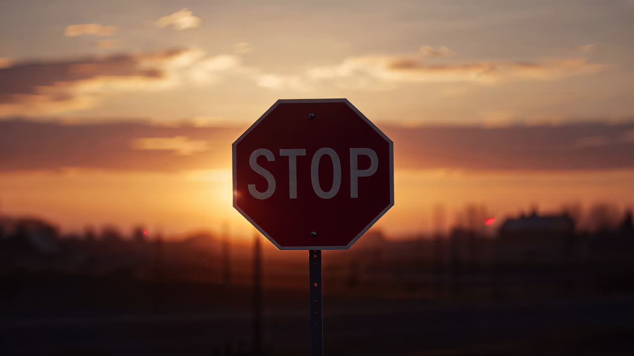 Sun lowering at sunset creating red octagonal STOP sign silhouette at roadside, shifting flare