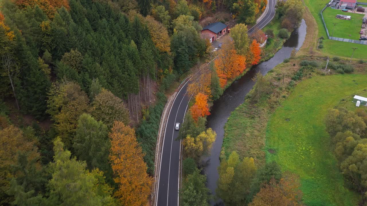 A car driving on a road in a rural landscape. The autumn colors of the trees invite you to go to nature to draw energy