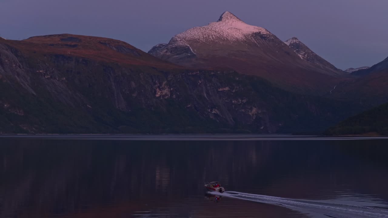 Ripresa aerea di un'imbarcazione che si muove rapidamente attraverso un fiordo al crepuscolo in Norvegia.