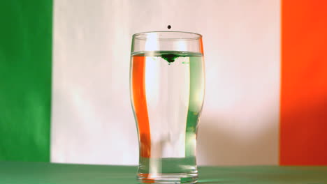 bandera irlandesa reflejada a través de un litro de agua con una gota verde cayendo en