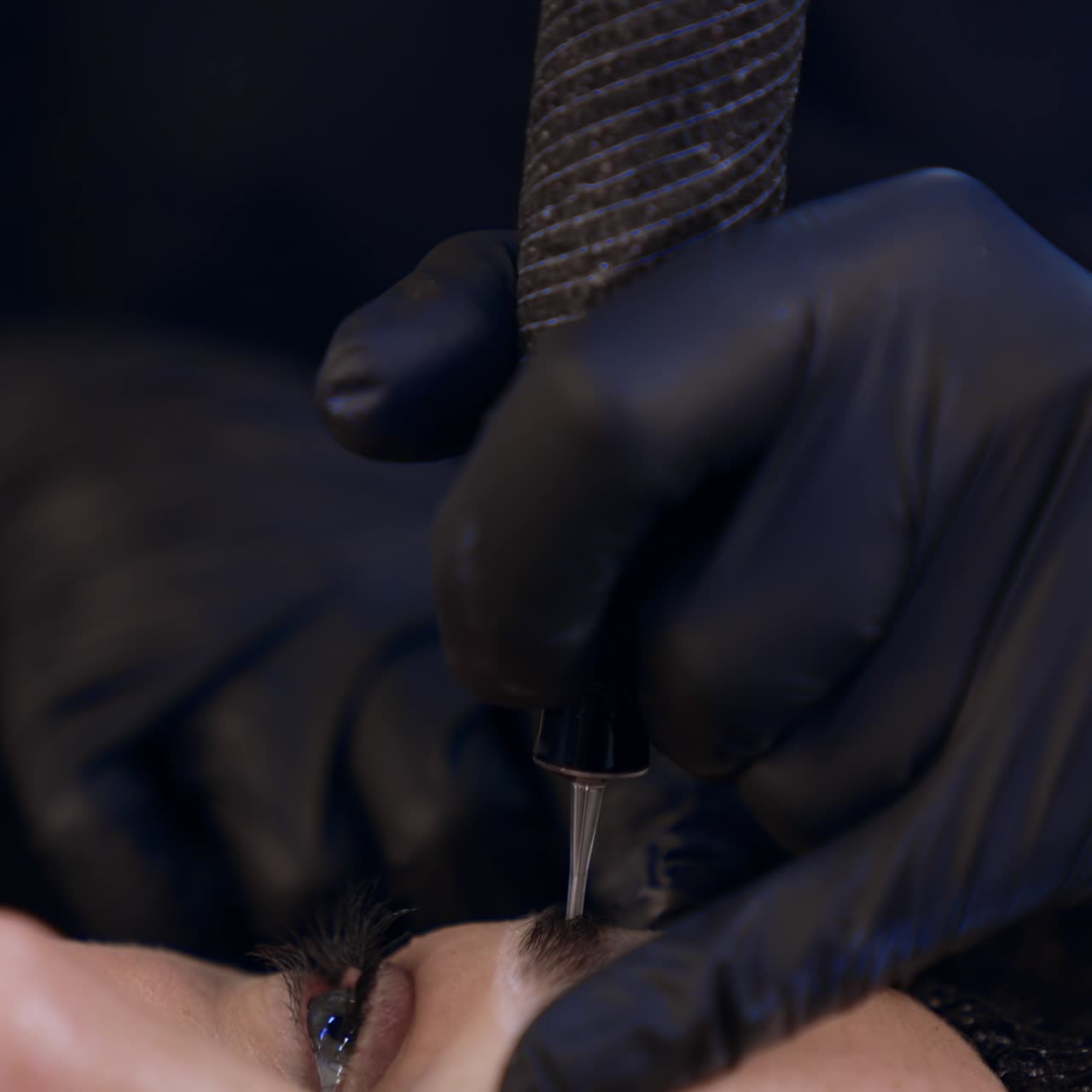 Tattooist's gloved hands use machine for eyebrow permanent. Make up at beauty salon. Close up
