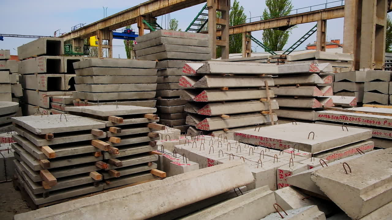 Ferroconcrete pallets and blocks piled together at the construction site. High metal construction supports at the backdrop.