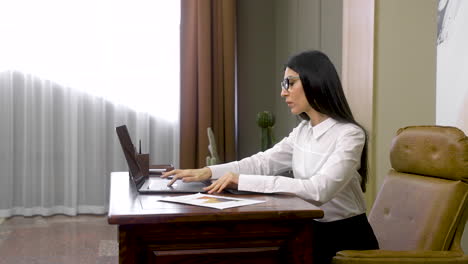 serious business woman working on laptop computer and then writing in the agenda while sitting at desk in the office