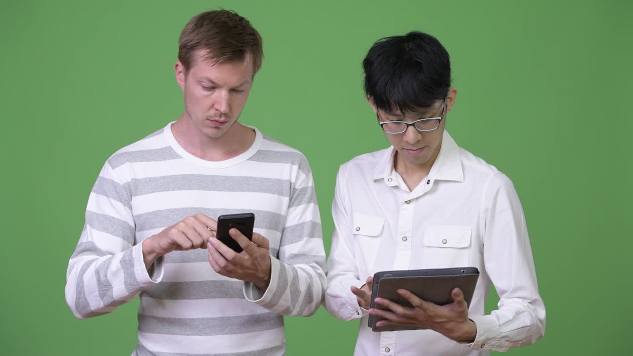 Two young multi-ethnic businessmen using phone and digital tablet for social media concept