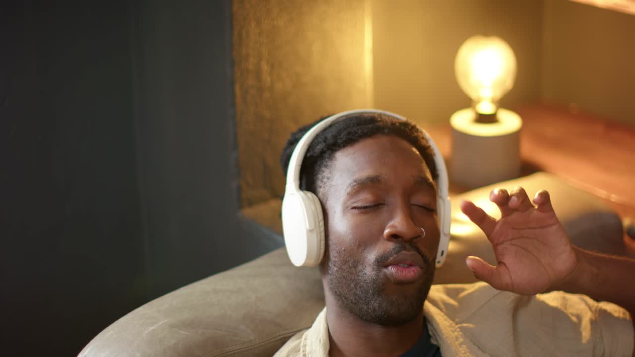 Uomo sdraiato a casa, che regola le cuffie bianche e mima le parole della musica che suona.