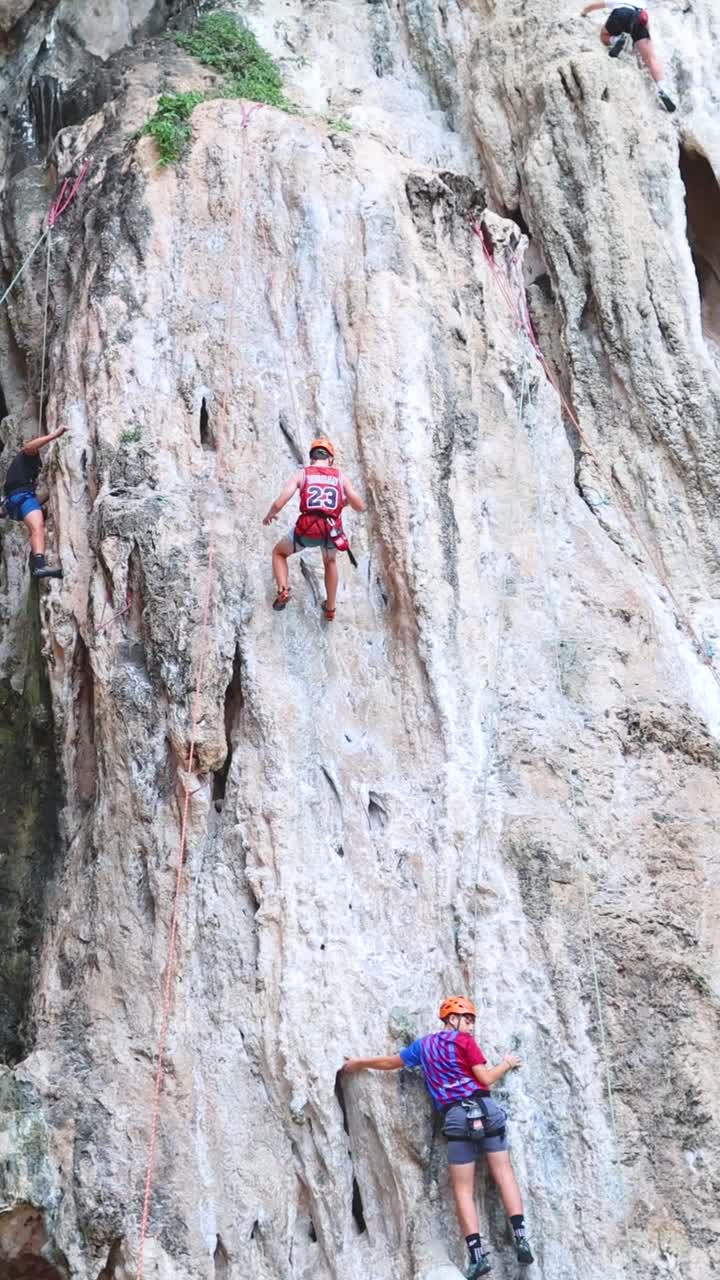 Multiple climbers ascend a textured limestone rock face using ropes and safety gear