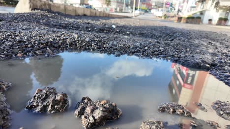 large pothole filled with water on a damaged asphalt road