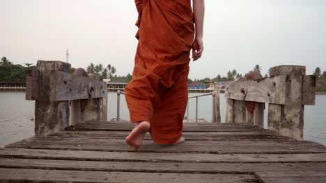 the monks are walking down to the waterfront using a wooden bridge