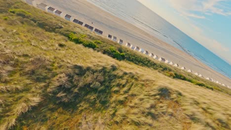 Fpv-Drone-Disparó-Volando-A-Alta-Velocidad-Sobre-Una-Playa-Vacía-Y-Dunas-Verdes-Cubiertas-De-Hierba-Durante-La-Puesta-De-Sol