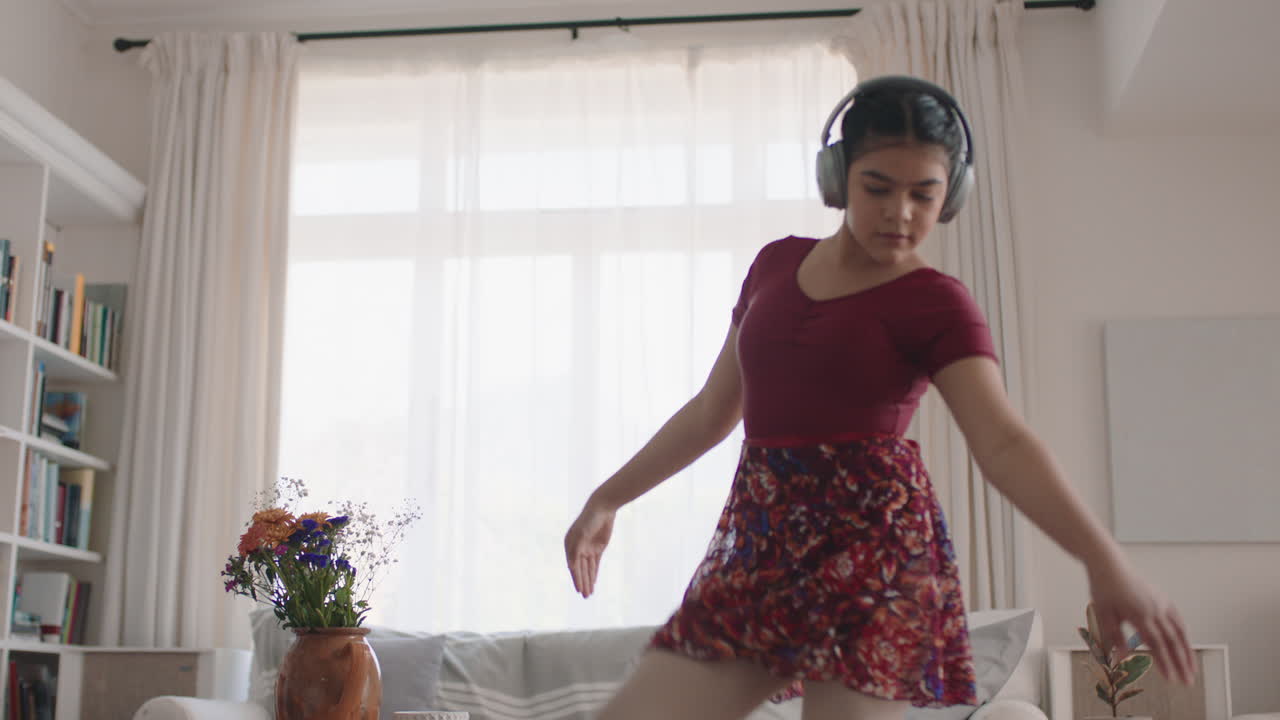 una adolescente feliz bailando practicando movimientos de ballet en casa escuchando música usando auriculares divirtiéndose disfrutando del fin de semana