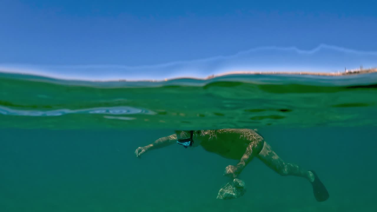 배경에 트라보치 낚시 플랫폼이 있는 해산물로 가득 찬 가방을 들고 있는 동안 마스크와 스노클링으로 조개와 홍합을 낚시하는 남자의 수중 오버 언더 뷰