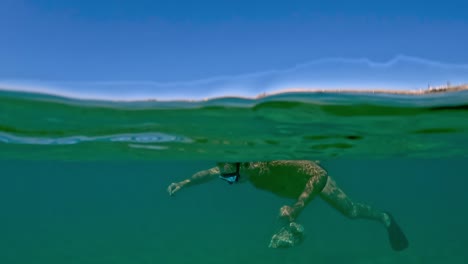 Halbe-Unterwassersicht-Auf-Einen-Mann,-Der-Muscheln-Und-Miesmuscheln-Mit-Maske-Und-Schnorchel-Fischt,-Während-Er-Eine-Tasche-Voller-Meeresfrüchte-Mit-Trabocchi-Fischerplattformen-Im-Hintergrund-Hält