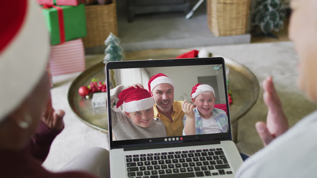 dos amigas mayores diversas que usan una computadora portátil para una videollamada de navidad con la familia en la pantalla