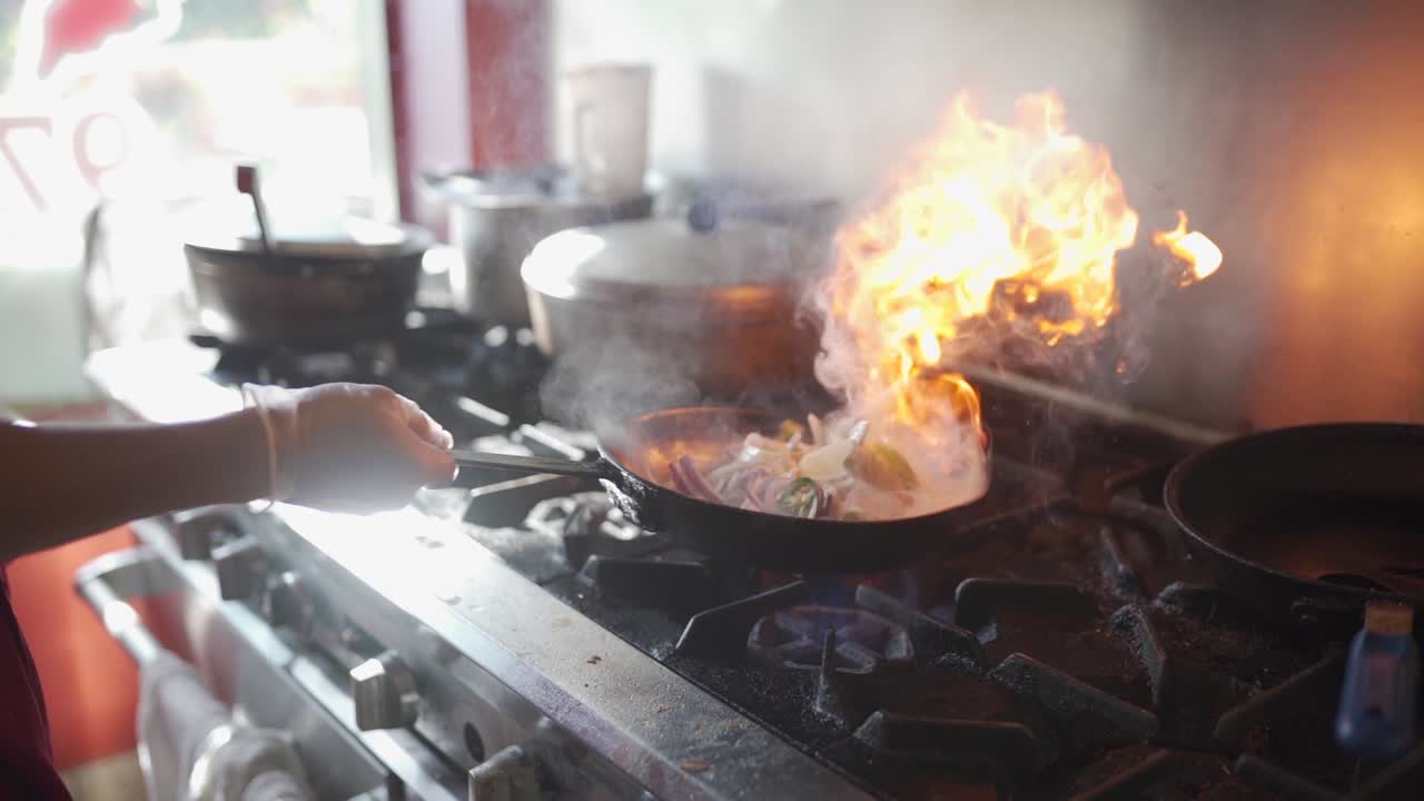 Flipping a pan with some vegetables in it, over a flame on the stove.