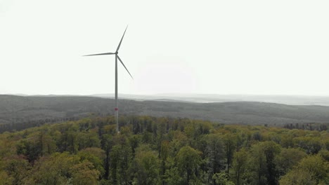Aerial-landscape-of-a-single-wind-turbine-spinning-on-top-of-a-hill,-surrounded-by-trees