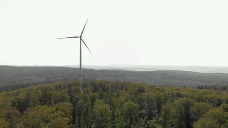 Paisaje-Aéreo-De-Un-Solo-Aerogenerador-Girando-En-La-Cima-De-Una-Colina,-Rodeado-De-árboles