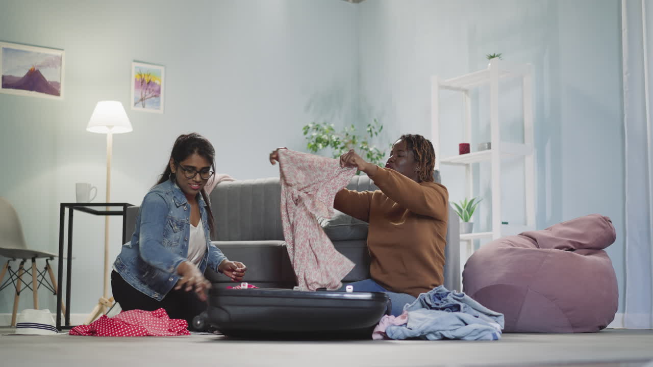 Happy multiracial friends put dresses into tourist suitcase