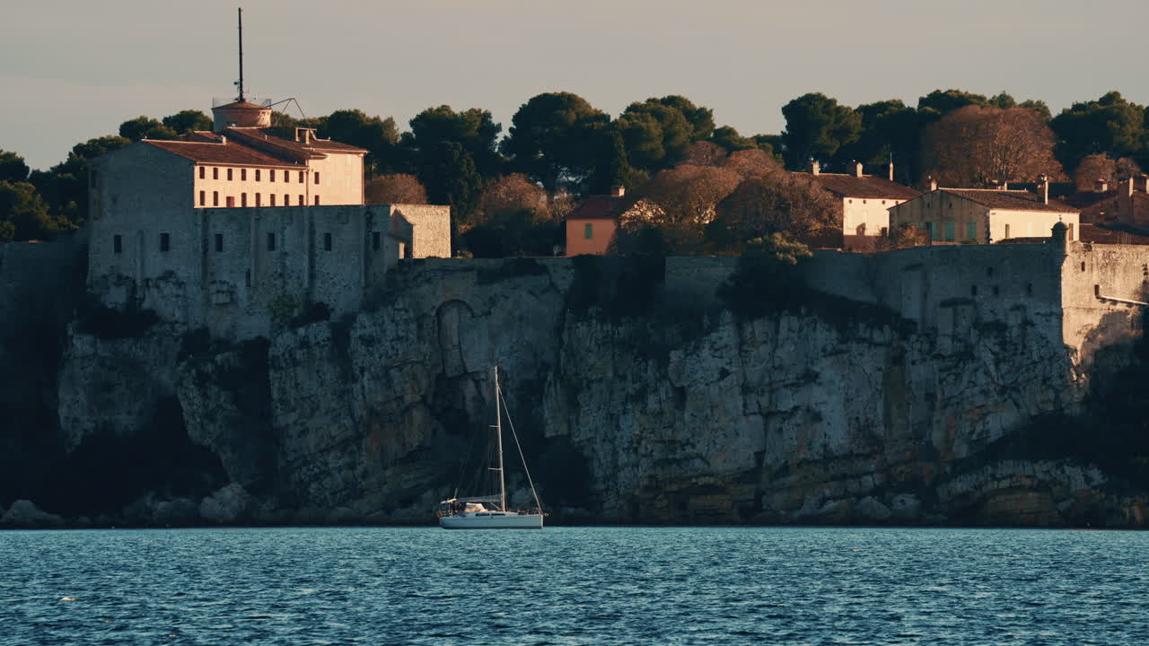 Barca a vela che galleggia sulle calme acque del Mediterraneo di fronte allo storico Fort Carré ad Antibes