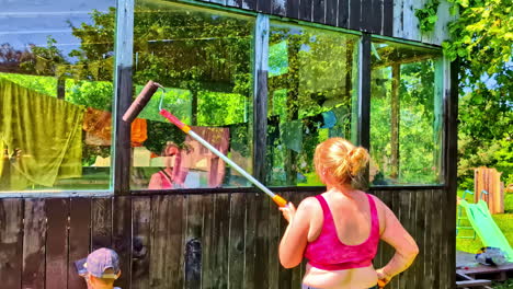 woman and children painting wooden wall of the house on sunny summer day