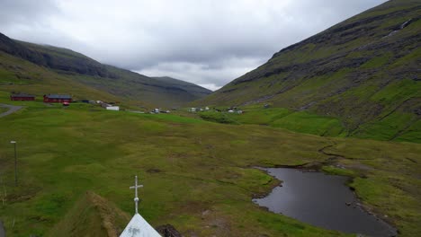 drone flying backwards revealing a faroese christian turf roof church in saksun