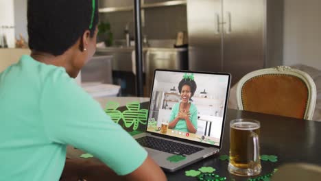 mujer afroamericana sonriente con cerveza vistiendo banda en forma de trébol en una llamada de video en una computadora portátil
