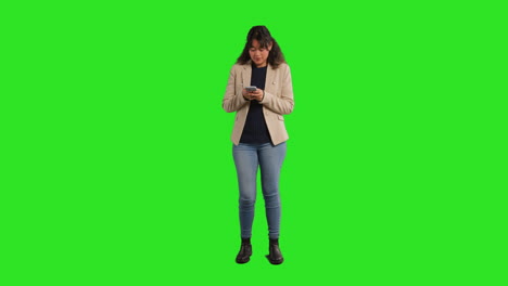 retrato de estudio de longitud completa de una maestra o mujer de negocios de pie contra una pantalla verde usando un teléfono móvil para enviar mensajes o navegar en línea 2