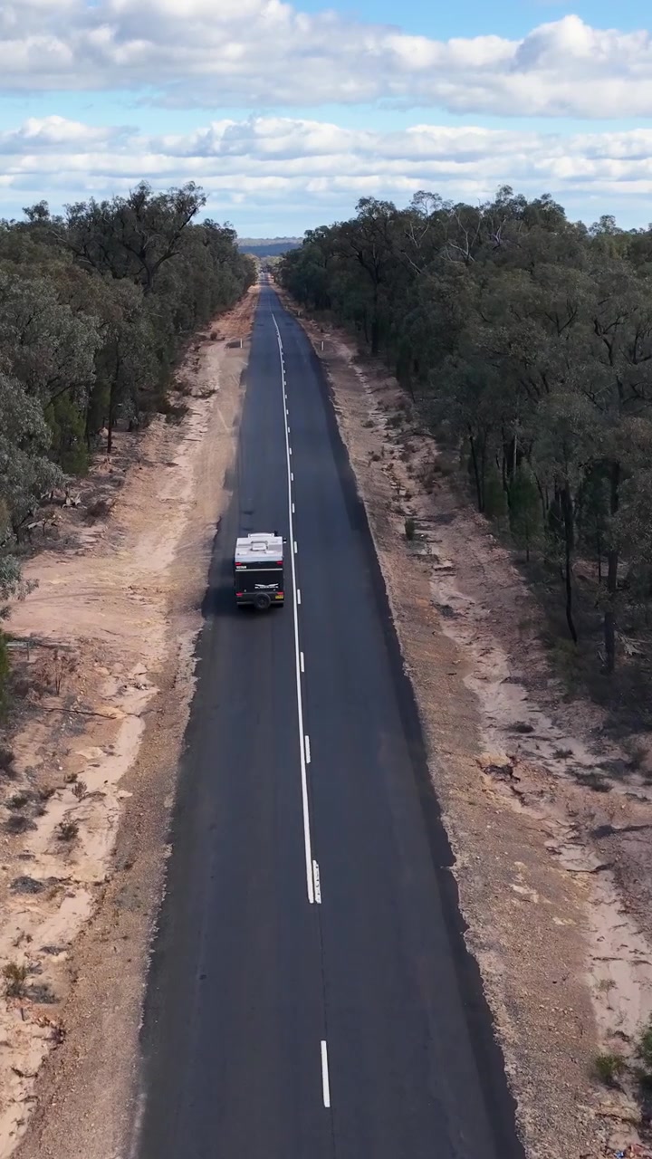 Ripresa aerea con drone di una roulotte che viaggia lungo una strada remota in Australia
