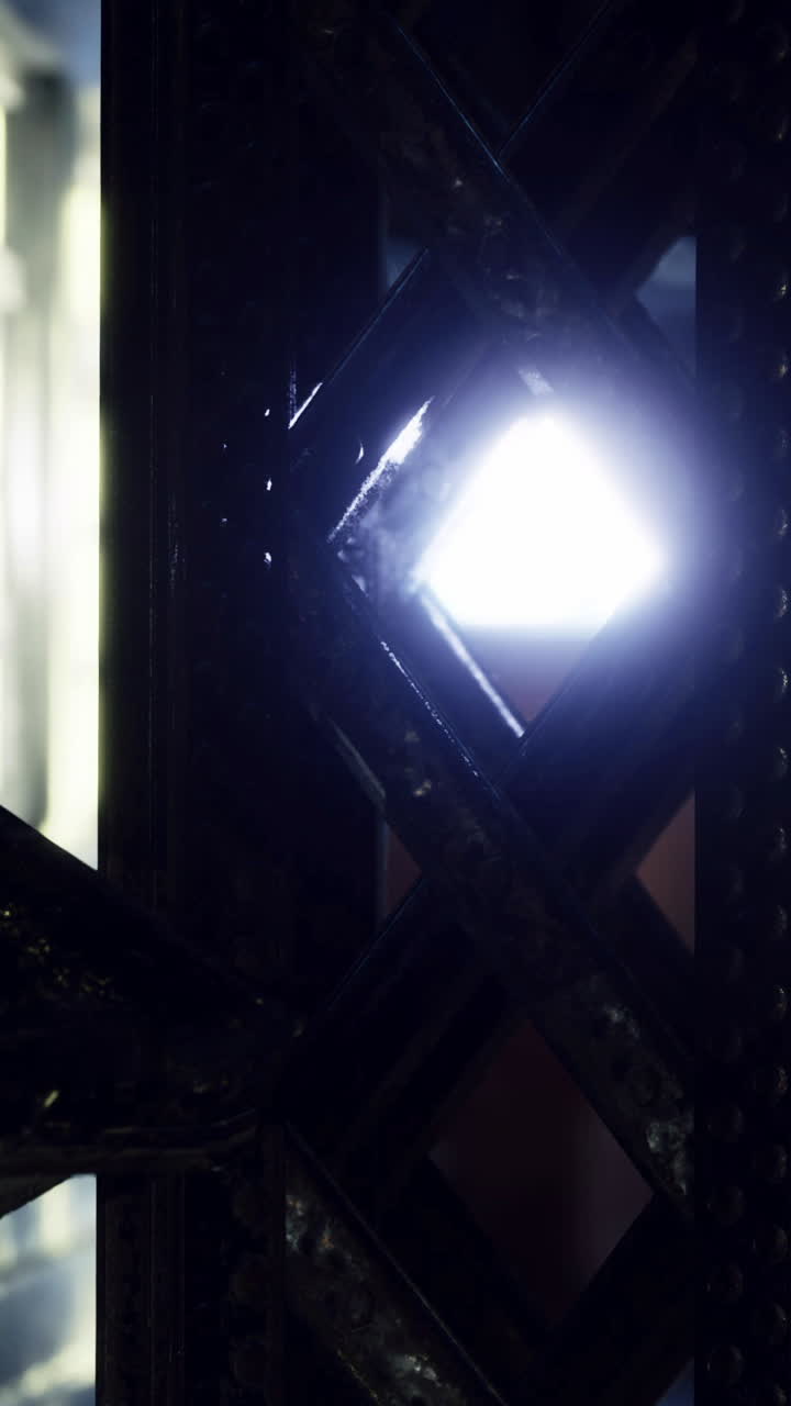 Luz brillando a través de una estructura de celosía en un espacio oscuro durante la noche.