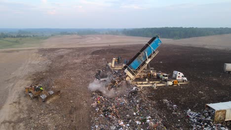 landfill site with trucks and machinery dumping and spreading waste in a large open area