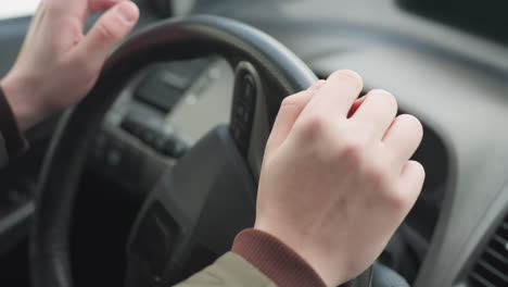 close up of driver placing both hands on steering wheel and gently tapping, indoor shot inside parked car with soft light, dashboard and wheel in focus while background fades subtly