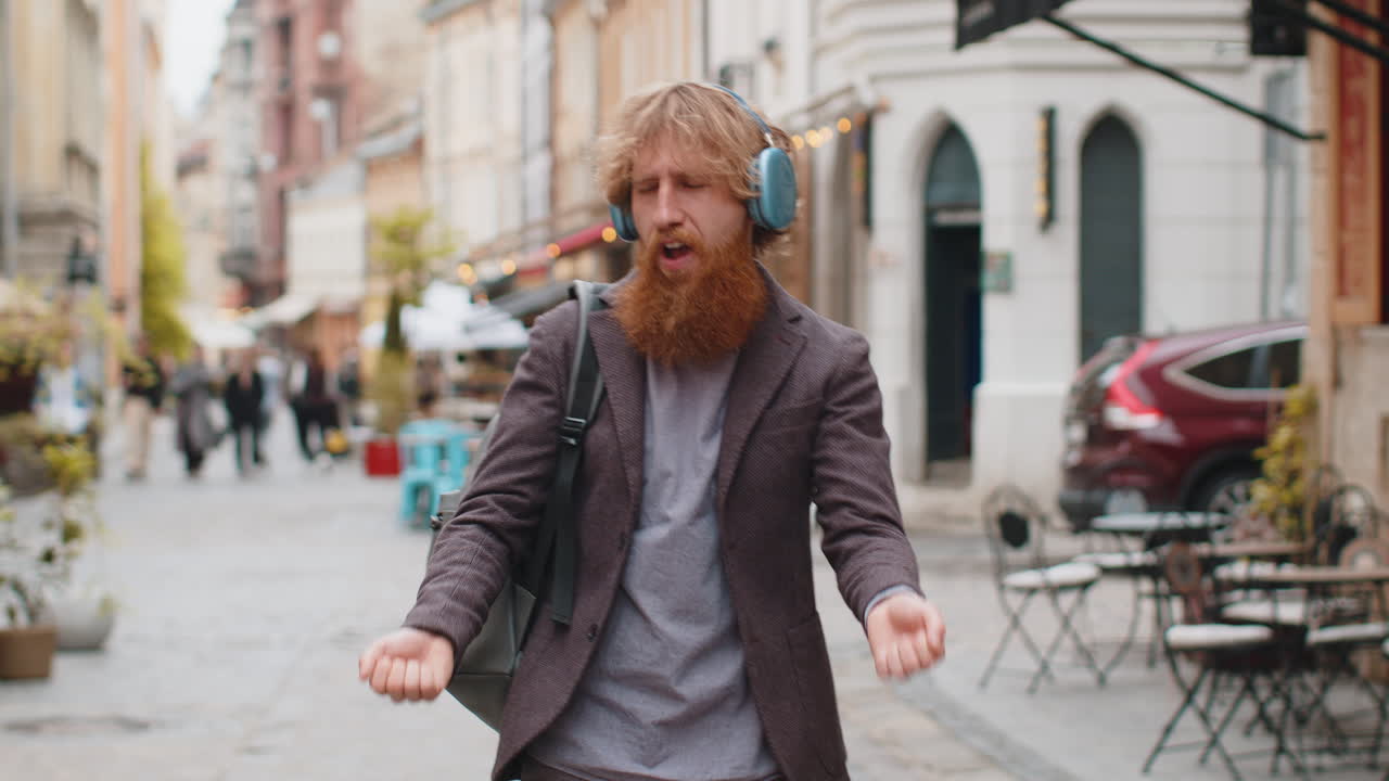 Happy young man in wireless headphones listening favorite energetic music in urban city street