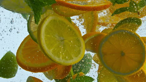 Stücke-Von-Zitrusfrüchten-Mit-Minze-In-Wasser-Fallen-Gelassen,-Nahaufnahme.-In-Scheiben-Geschnittene-Orange,-Zitrone,-Limette