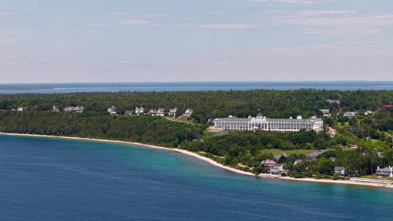 Droneudsigt langs en skovklædt kystlinje ved Hessel, Michigan, med huse ved søen og et stort feriested ved vandet ud til det blå Great Lakes-vand