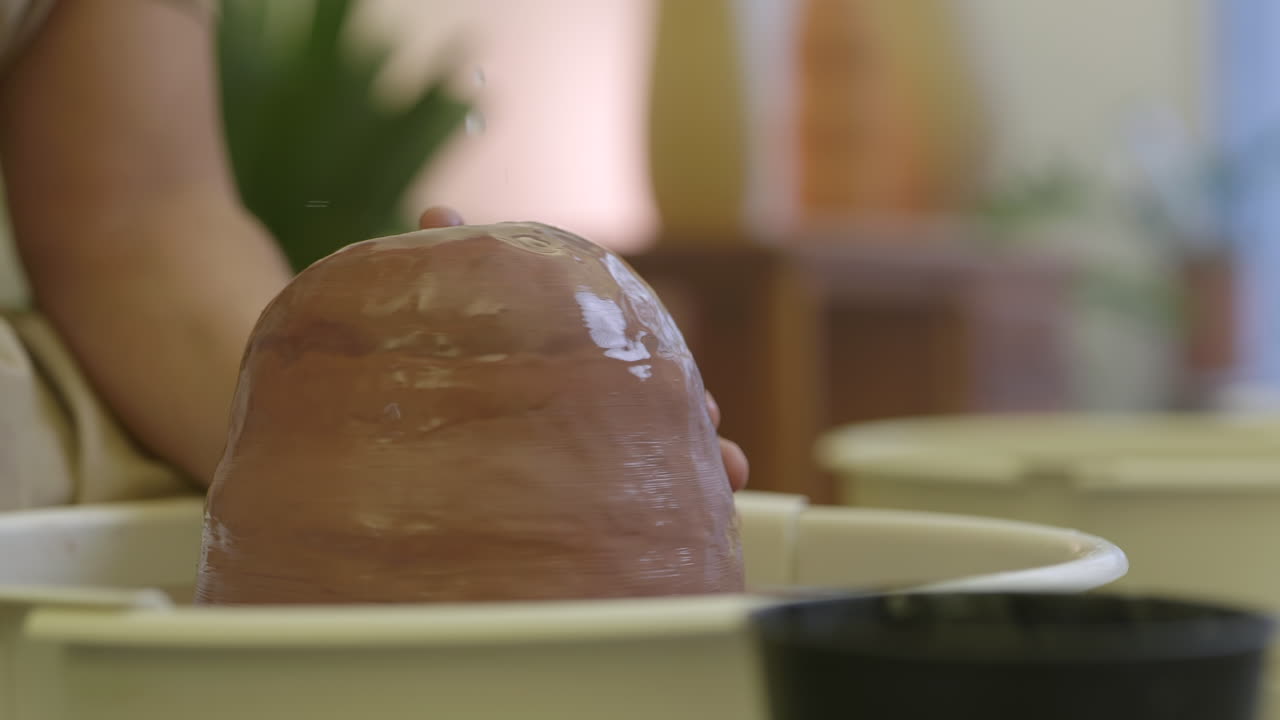 agua rociando sobre el montículo de arcilla cruda girando en la rueda de cerámica preparándose para dar forma al recipiente